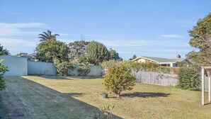 A backyard with a small tree, a wooden fence, and a house in the background. - Tura Beach Getaway on Telopea (Tura Beach)
