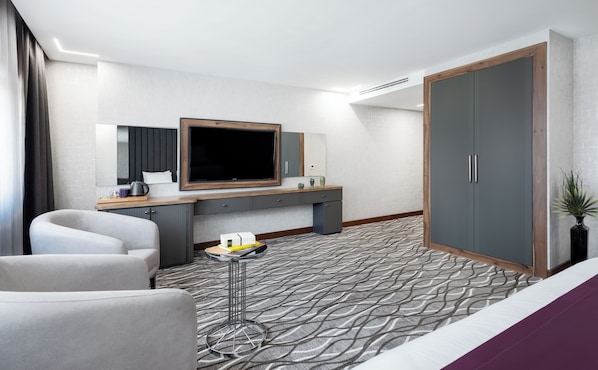 Une chambre d’hôtel moderne dotée d’un grand lit, d’un bureau avec un téléviseur à écran plat, d’un coin salon avec deux fauteuils et d’une armoire.