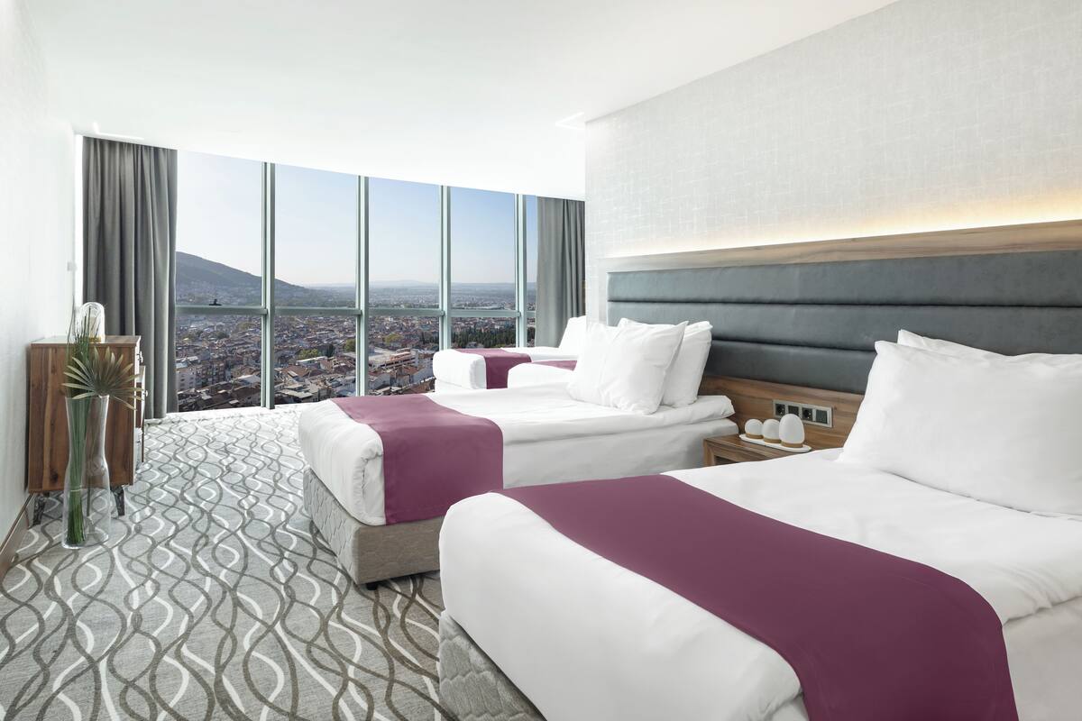 A hotel room with two beds, a large window with a city view, and a modern design.