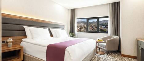Habitación de hotel con una cama grande, un escritorio pequeño, una silla y una ventana con vistas a la ciudad.