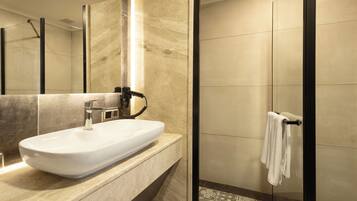Un baño moderno con un espejo grande, un lavamanos blanco y una cabina de ducha con paredes de cristal.