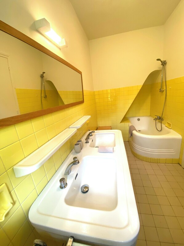 Baño con un lavamanos grande, una bañera y una ducha. Hay un espejo sobre el lavamanos y una repisa con artículos de aseo.