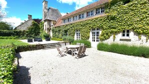 A stone building with ivy-covered walls, a gravel patio with outdoor furniture, and a stone chimney.