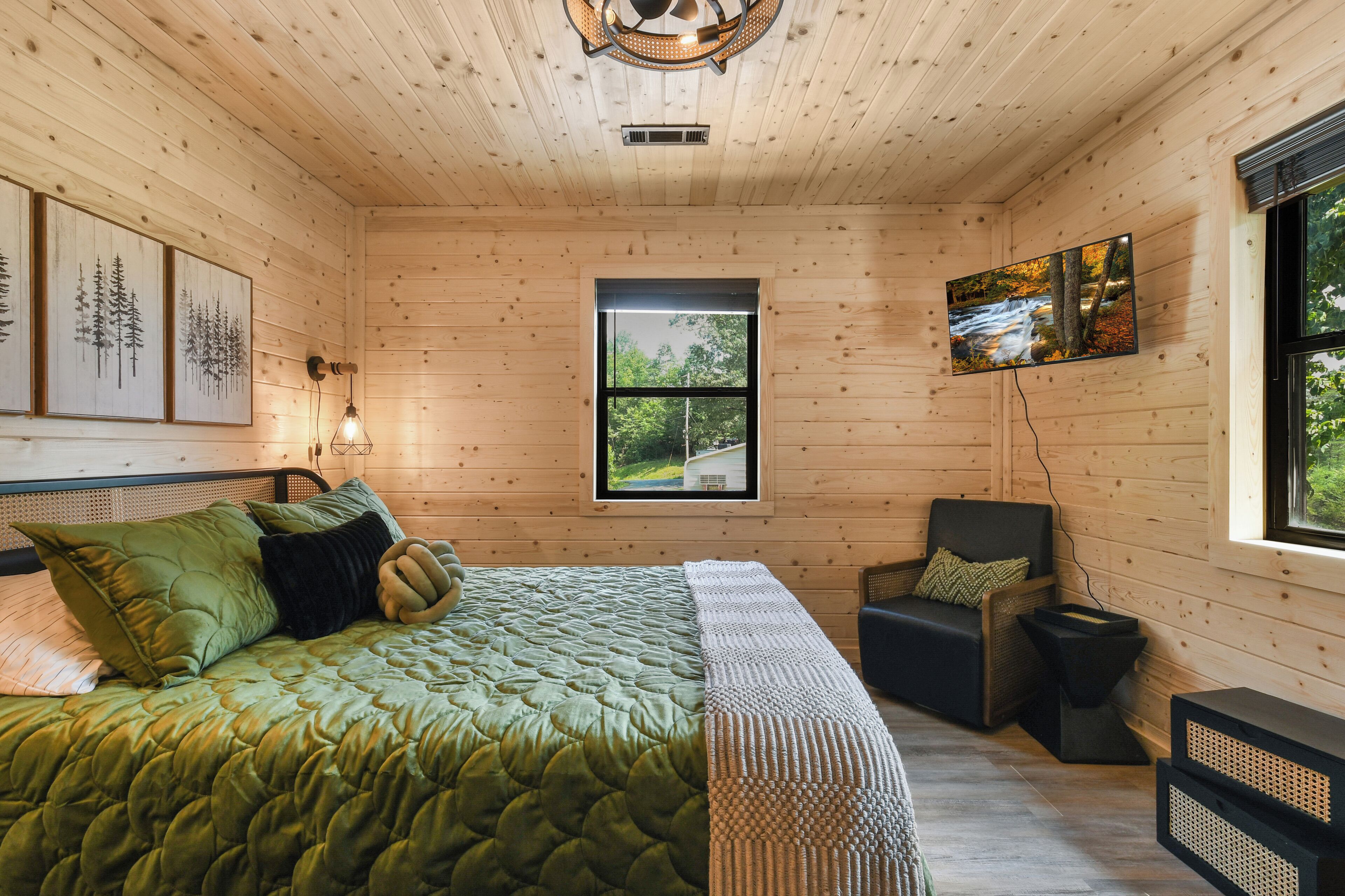 Une chambre dans une cabane en bois, avec un lit, une chaise, un téléviseur et une fenêtre donnant sur la forêt.