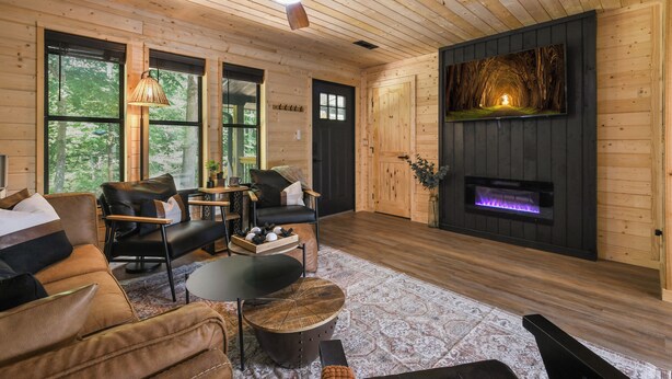 A cozy cabin interior with a wooden ceiling, a fireplace, leather furniture, and large windows. - Smokies Pond Escape/Secluded Mtn cabin w/pond/Fish’n/Hot tub/2 fenced yards/Pets (Pigeon Forge)