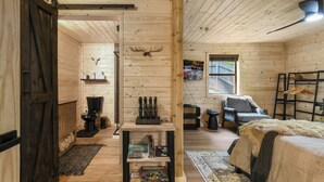 A cozy cabin interior with wooden walls, a bed with a fur throw, a fireplace, and a game shelf. - Smokies Pond Escape/Secluded Mtn cabin w/pond/Fish’n/Hot tub/2 fenced yards/Pets (Pigeon Forge)