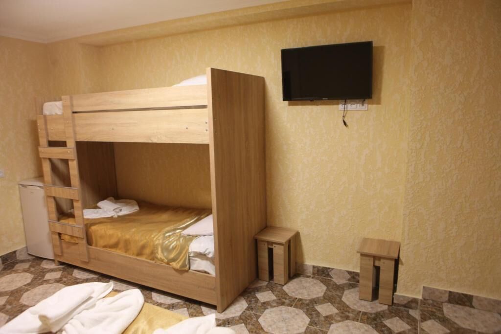 A bunk bed with a ladder, a small bedside table, a television mounted on the wall, and a tiled floor.