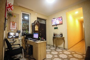 A hotel room with a wooden desk, a computer, a television, and a small table with bottles. - Hotel WB (Kutaisi)