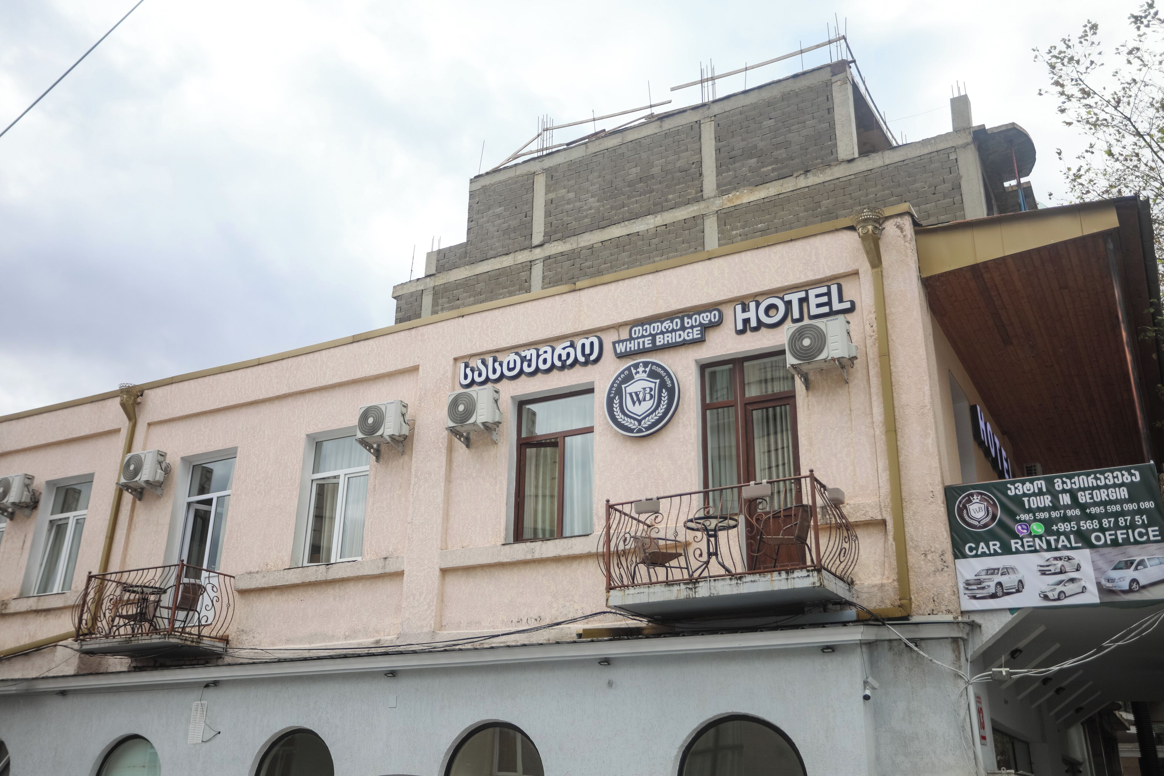 A hotel with balconies, air conditioning units, and a sign for a car rental office.