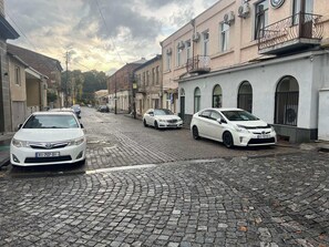 A cobblestone street lined with buildings, some with balconies and air conditioning units.