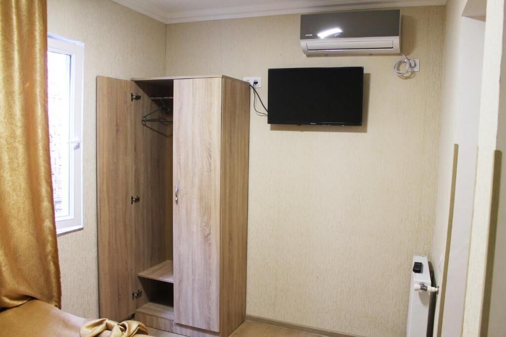 A room with a wooden wardrobe, a mounted TV, and an air conditioning unit.