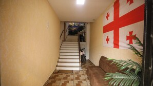 A hallway with a staircase, a brown couch, and a wall with a flag. - Hotel WB (Kutaisi)