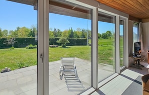 A room with large sliding glass doors leading to a grassy outdoor area, a bench, and a television on a wooden stand.