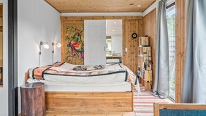 Un dormitorio con cama de madera, un ventanal con cortinas, un armario de madera y un estante en la pared con herramientas.