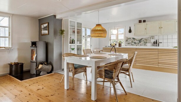 Een moderne keuken met witte kasten, een mozaïek spatwand en een eethoek met een witte tafel en rieten stoelen.