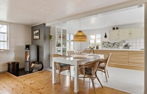 A modern kitchen with white cabinets, a mosaic backsplash, and a dining area with a white table and wicker chairs.