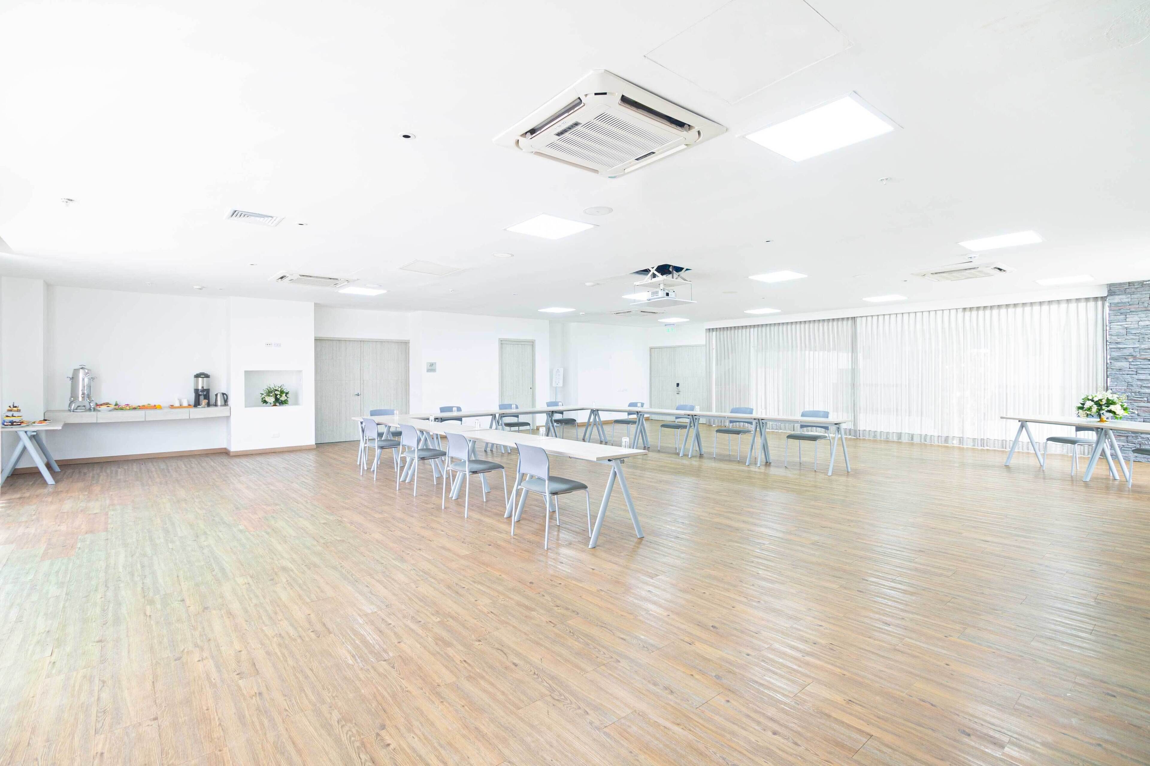 Una espaciosa sala de conferencias con largas mesas y sillas, paredes blancas y piso de madera.