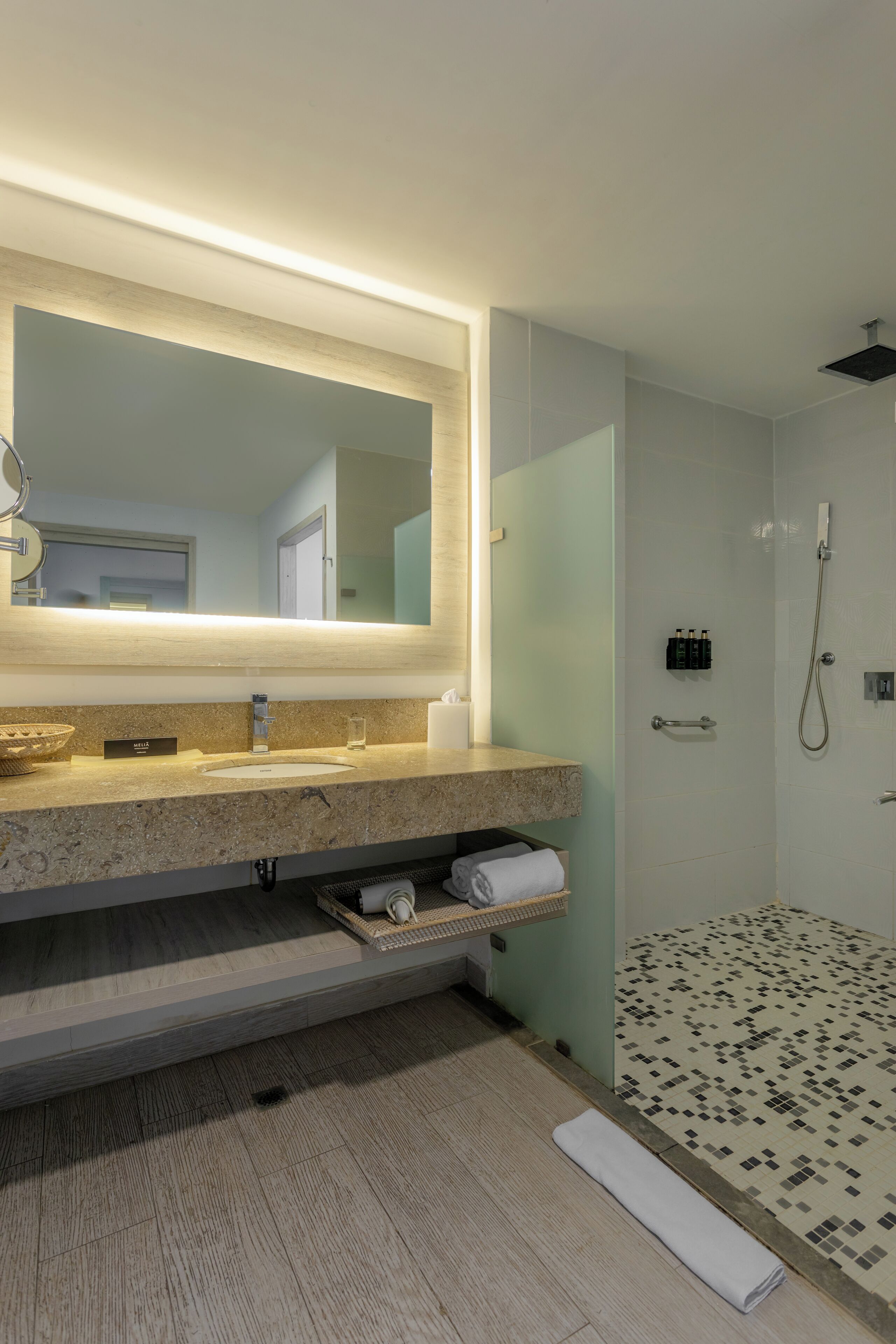 A modern bathroom with a large mirror, a sink, a shower, and a towel rack.