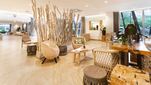 Een ruime lobby met modern meubilair, een houten bijzettafeltje en een groot raam met uitzicht op de omgeving.