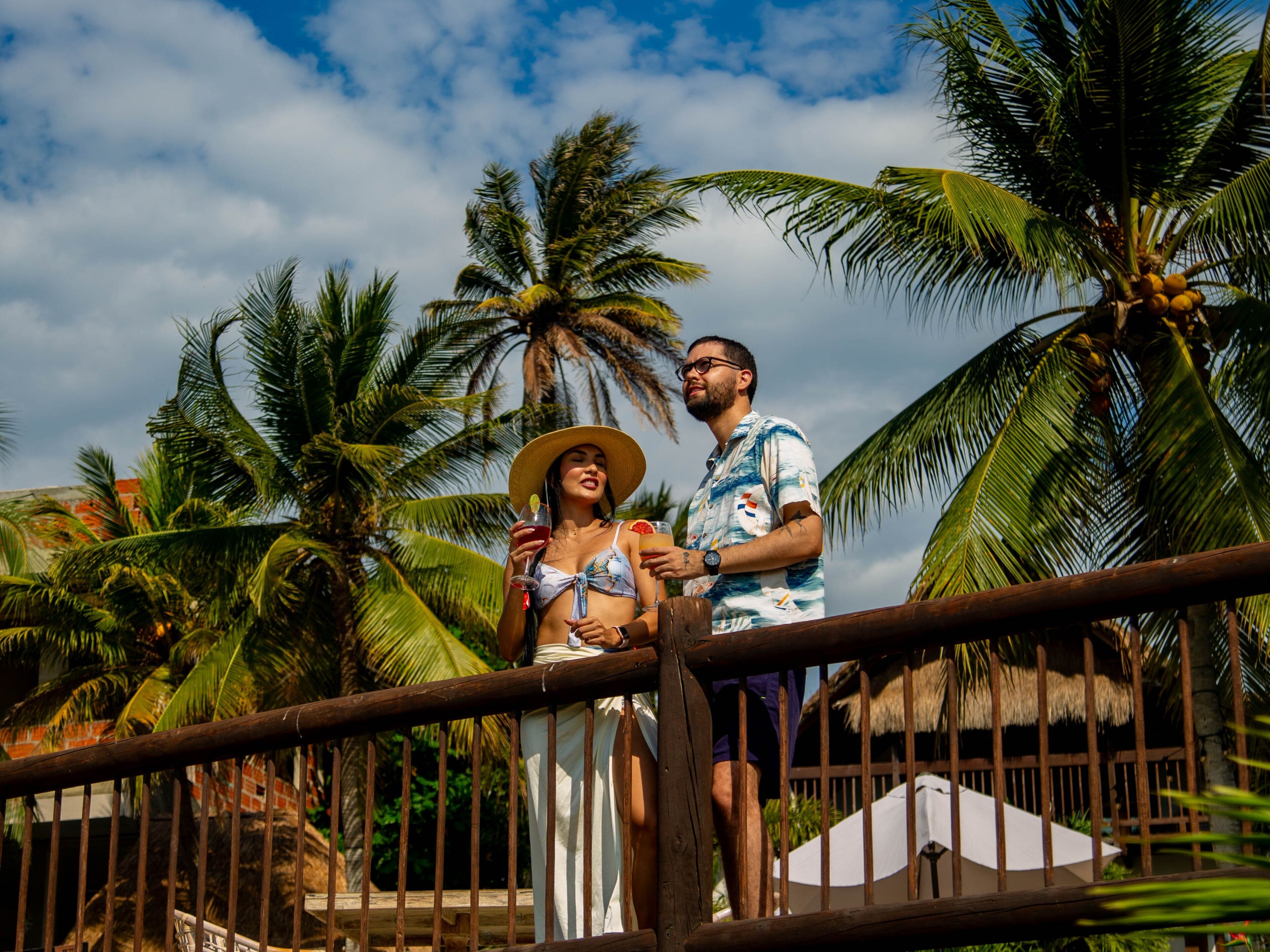 A couple standing on a wooden deck with palm trees in the background.