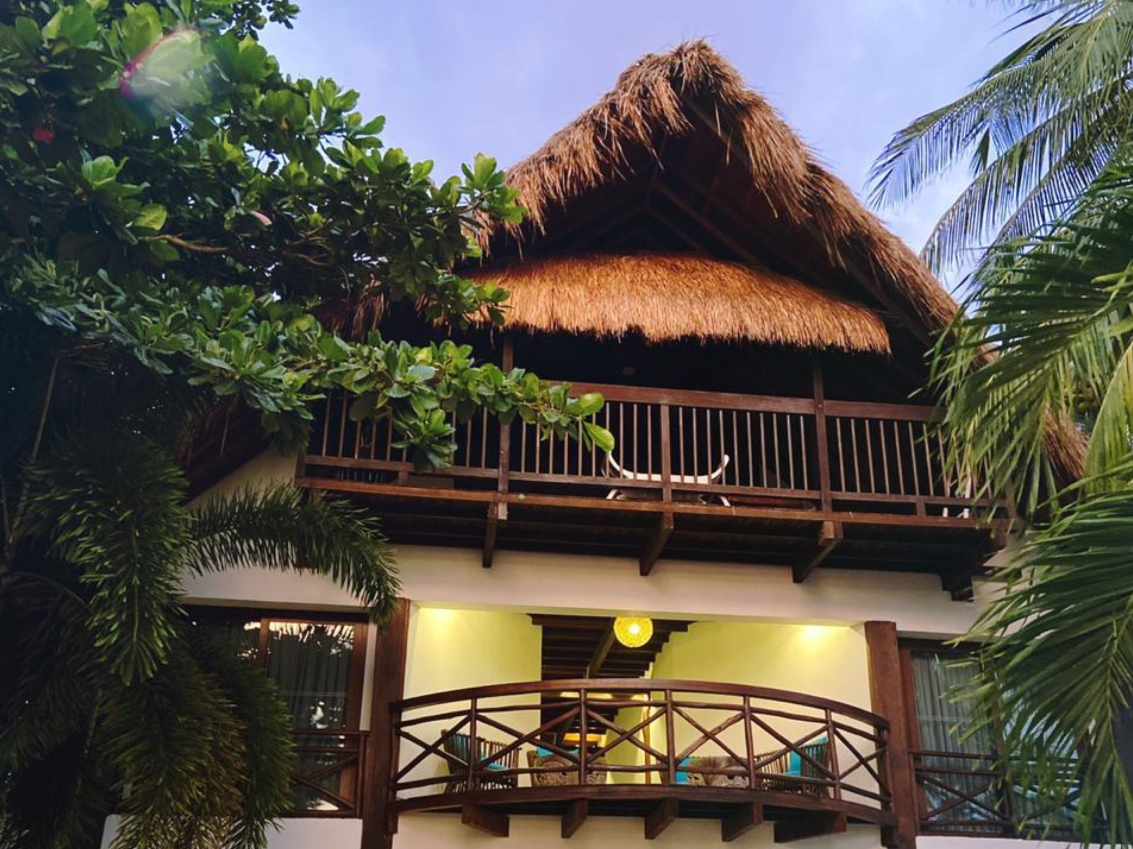 A two-story building with a thatched roof, a balcony with wooden railings, and a staircase leading to the upper floor.