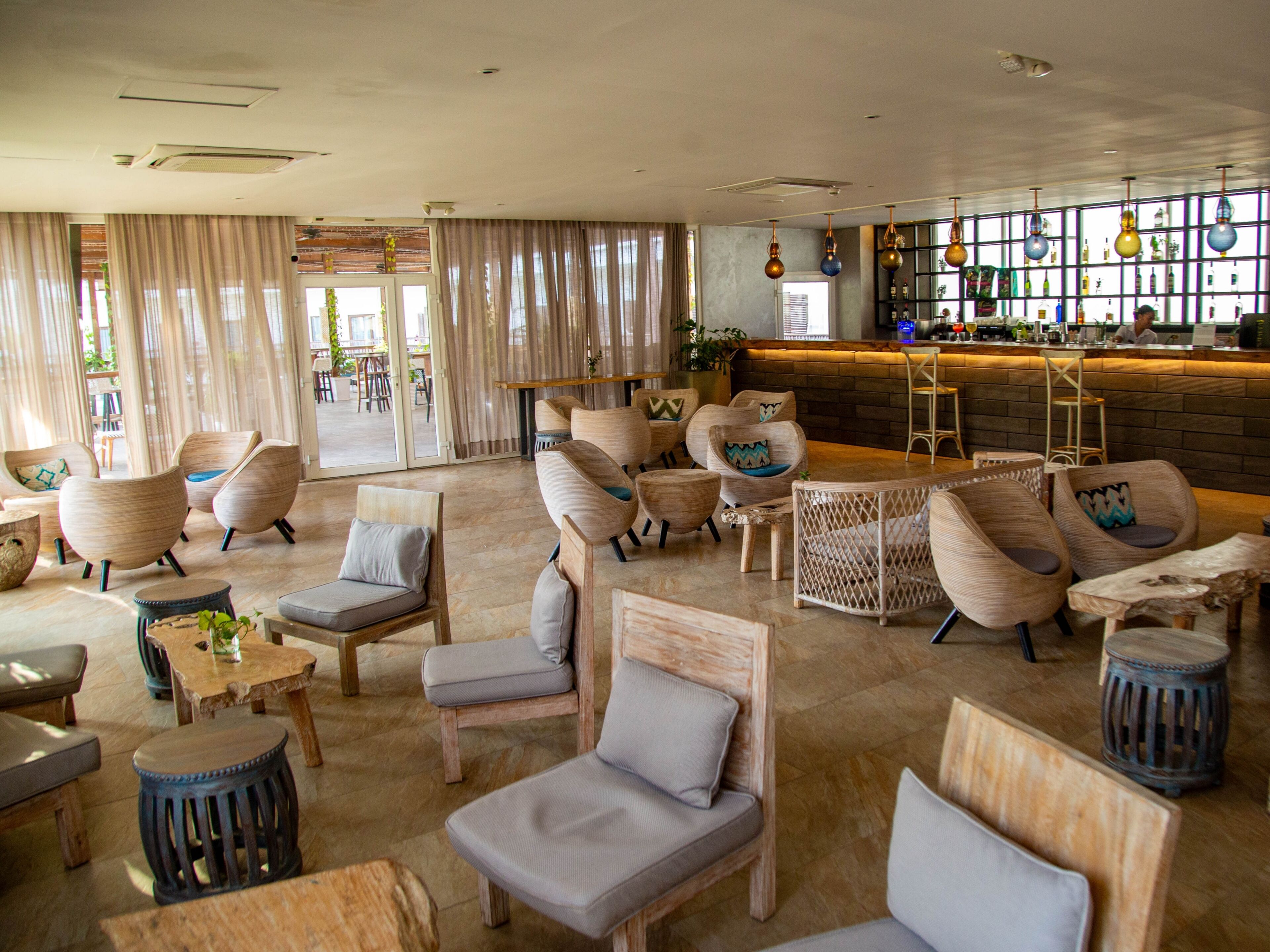 Un vaste espace salon offrant de nombreuses options d’assises, notamment des canapés et des fauteuils, un coin bar avec un comptoir, et une vue dégagée grâce à de grandes fenêtres.