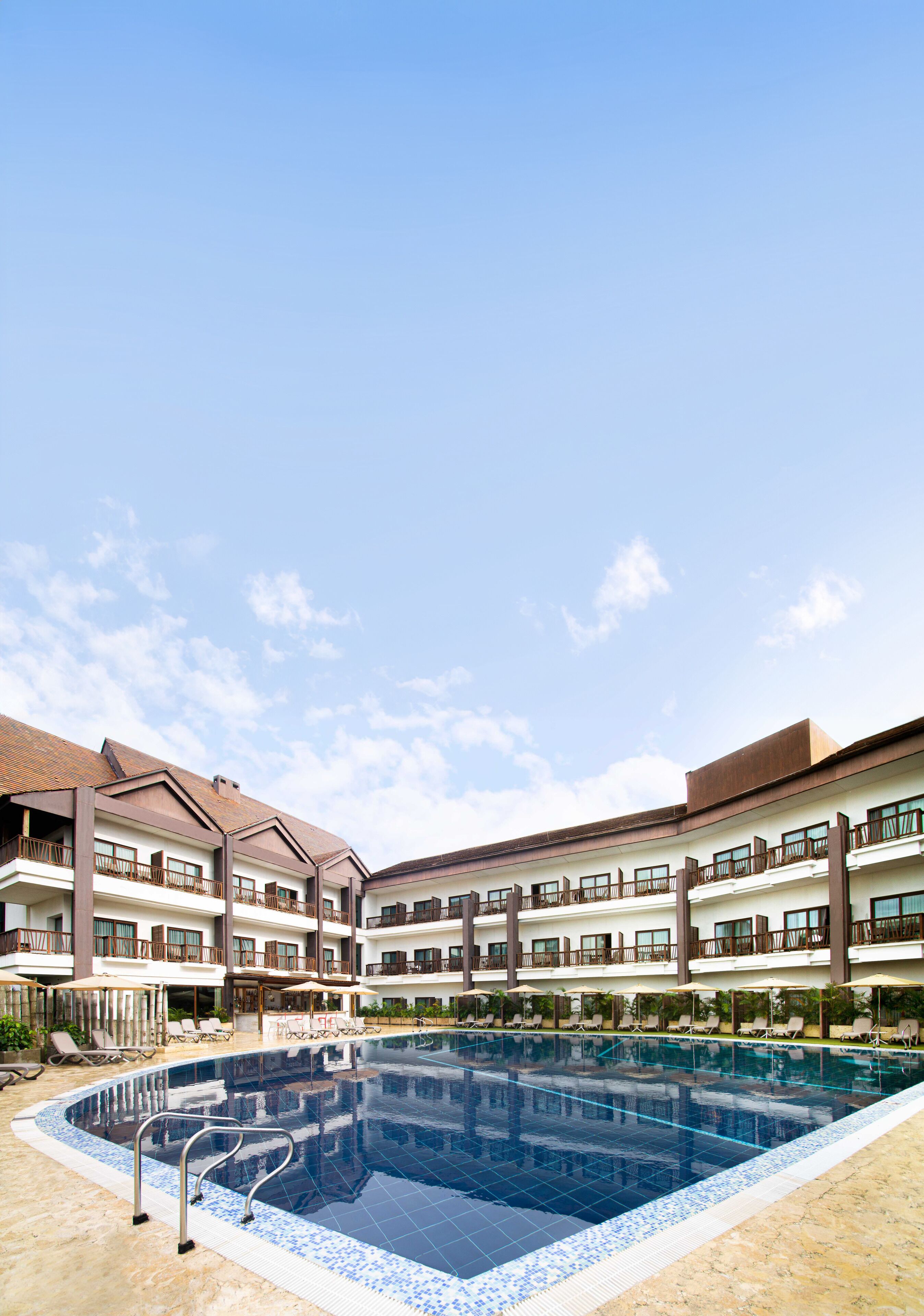 Un hotel con una piscina amplia, varios balcones y tumbonas.