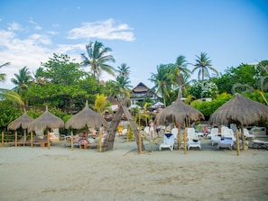 A beach resort with thatched umbrellas, lounge chairs, and palm trees. - Grand Sirenis Cartagena (Cartagena)
