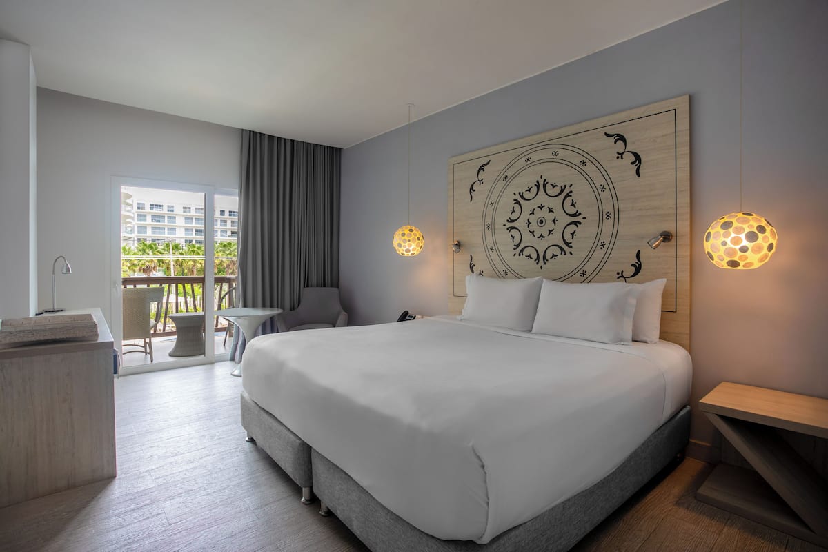 A hotel room with a large bed, a desk, a chair, and a view of the outdoors.