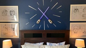 Ett sovrum med en stor väggklocka, kuddar med Star Wars-motiv och två sänglampor.