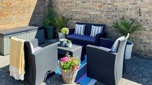 Une terrasse avec des meubles d’extérieur, un mur en briques et des plantes en pot.