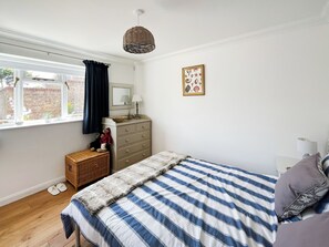 A bedroom with a bed, dresser, window, and a decorative wall piece.