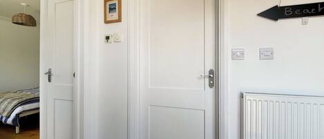 Una habitación con dos puertas blancas, un pequeño cuadro en la pared, un termostato y un cartel que indica el camino a la playa.