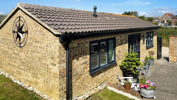 Une maison en briques avec un toit en tuiles, une boussole accrochée au mur et des plantes en pot.