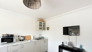 Une cuisine avec des meubles blancs, un four à micro-ondes, un grille-pain, un évier et un téléviseur fixé au mur.