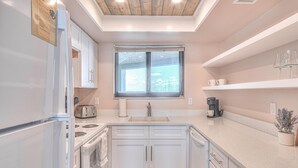 A modern kitchen with white cabinetry, a built-in oven, a stovetop, and a window above the sink. - Ocean Trillium 803 - a 1 bedroom condo with beautiful ocean views (New Smyrna Beach)