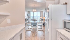 A modern kitchen with white cabinetry, a central island with seating, and a view to the outside. - Ocean Trillium 803 - a 1 bedroom condo with beautiful ocean views (New Smyrna Beach)