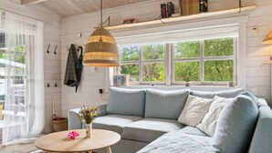 Una sala de estar acogedora con un sofá gris, una mesa redonda de madera y una lámpara colgante.