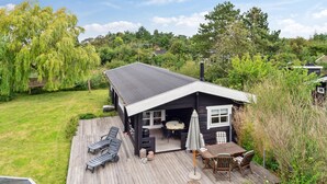 Una cabaña de madera con terraza, un patio amueblado al aire libre y vistas de la vegetación circundante.