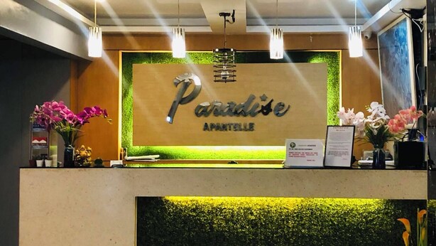 Un mostrador de recepción con un letrero que dice "Paradise Apartelle" y una pared verde con textura similar a la hierba.