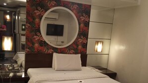 Habitación de hotel con cama, espejo redondo, televisor y aire acondicionado instalado en la pared.