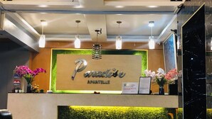 Una recepción con un cartel que dice "Paradise Apartelle", iluminación colgante y una pared verde con plantas.