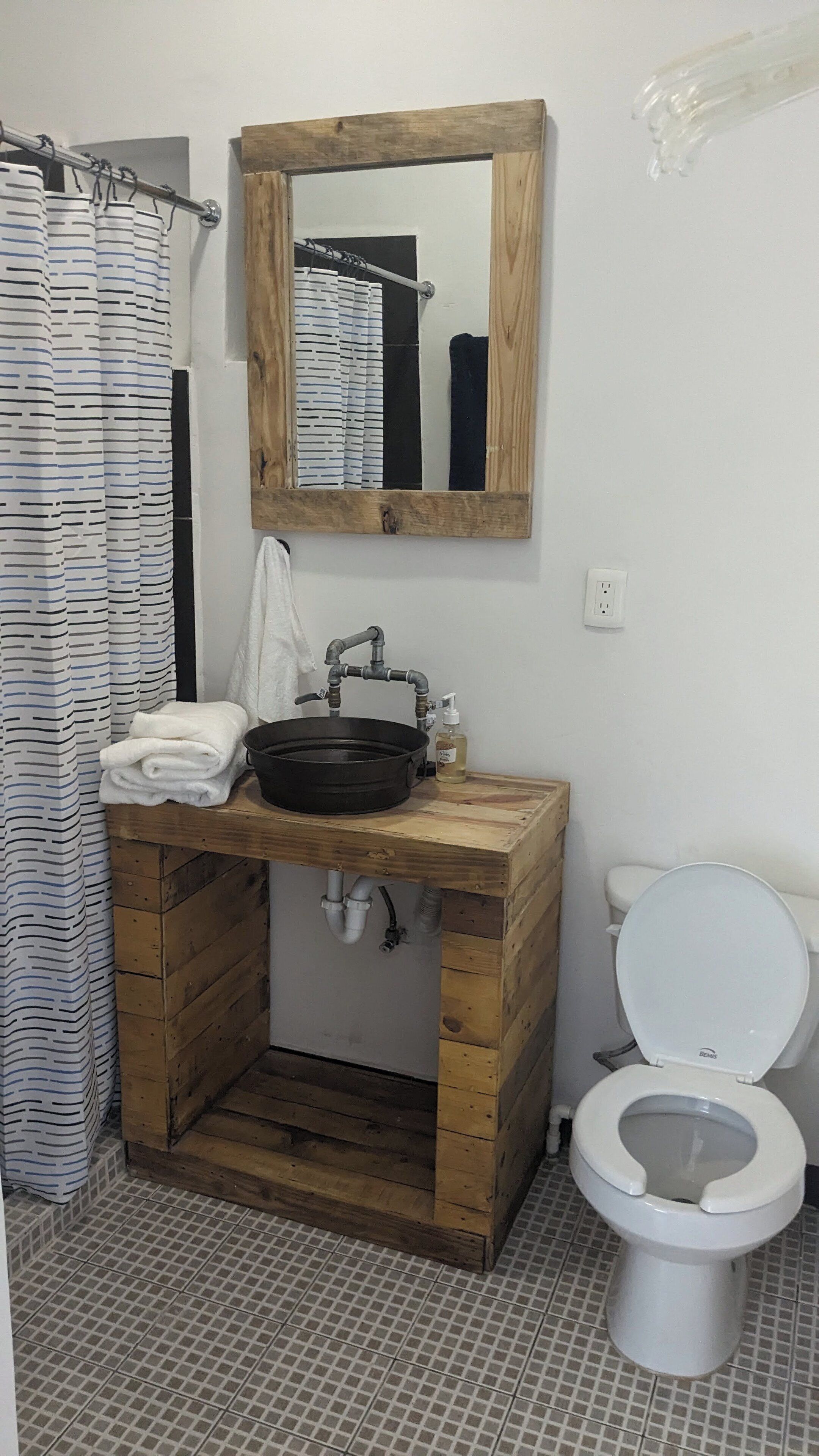 Un baño con tocador de madera, lavabo, espejo, inodoro y cortina de ducha.