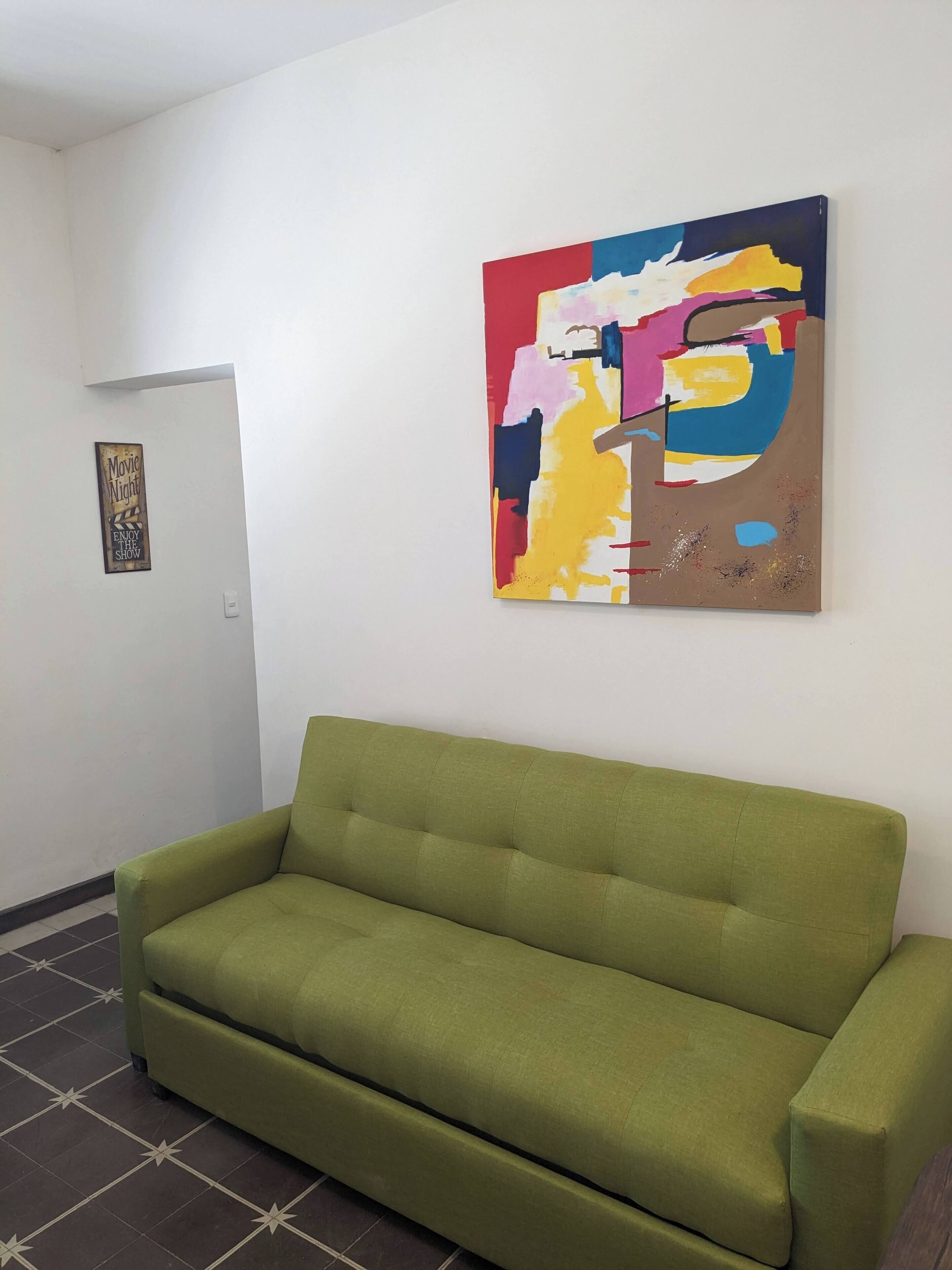 Un sofá verde en una habitación con un cuadro abstracto de colores en la pared y un letrero que dice "Movie Night".