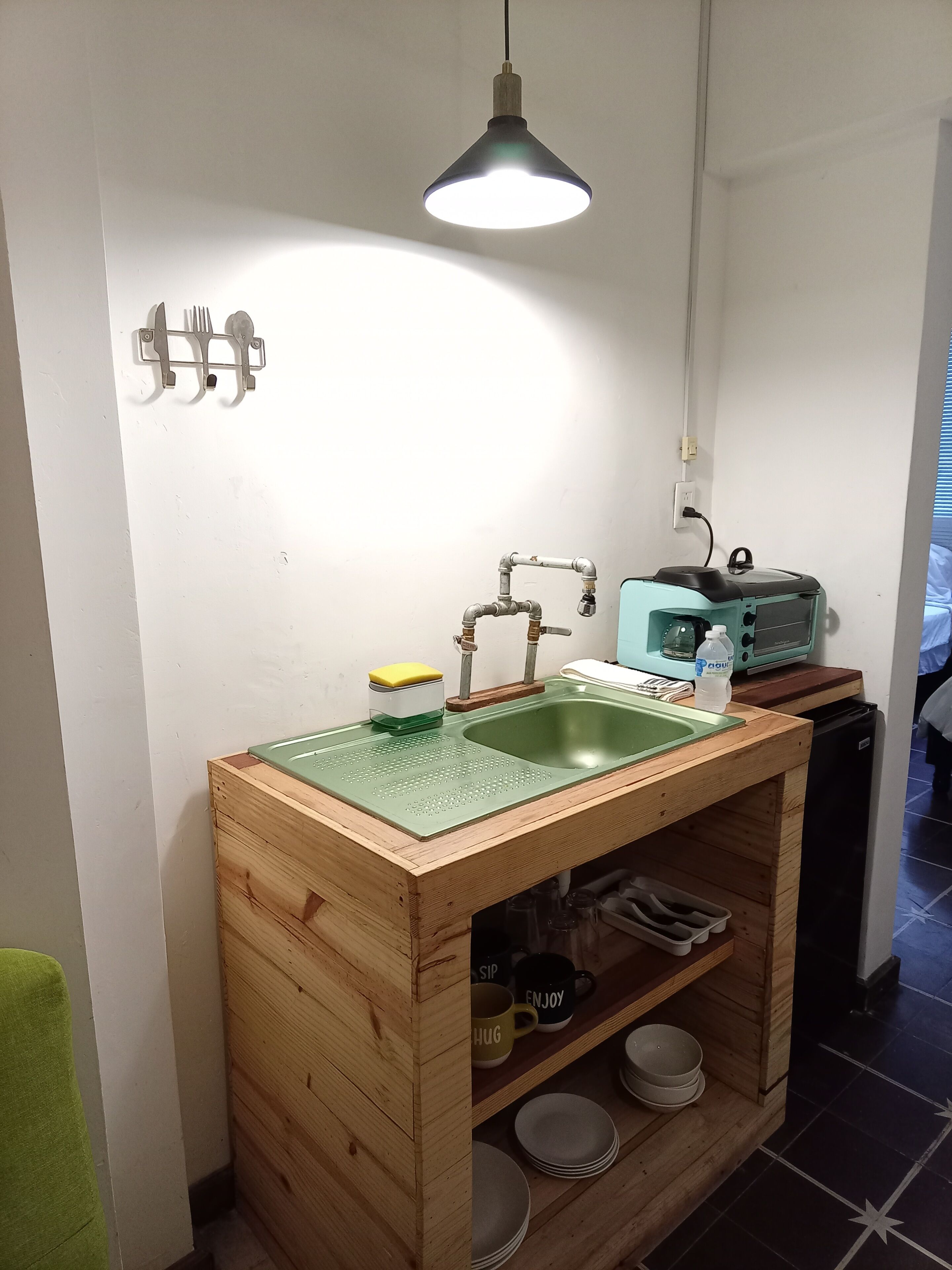 A compact kitchen with a wooden countertop, a sink, a hanging light, and a toaster.