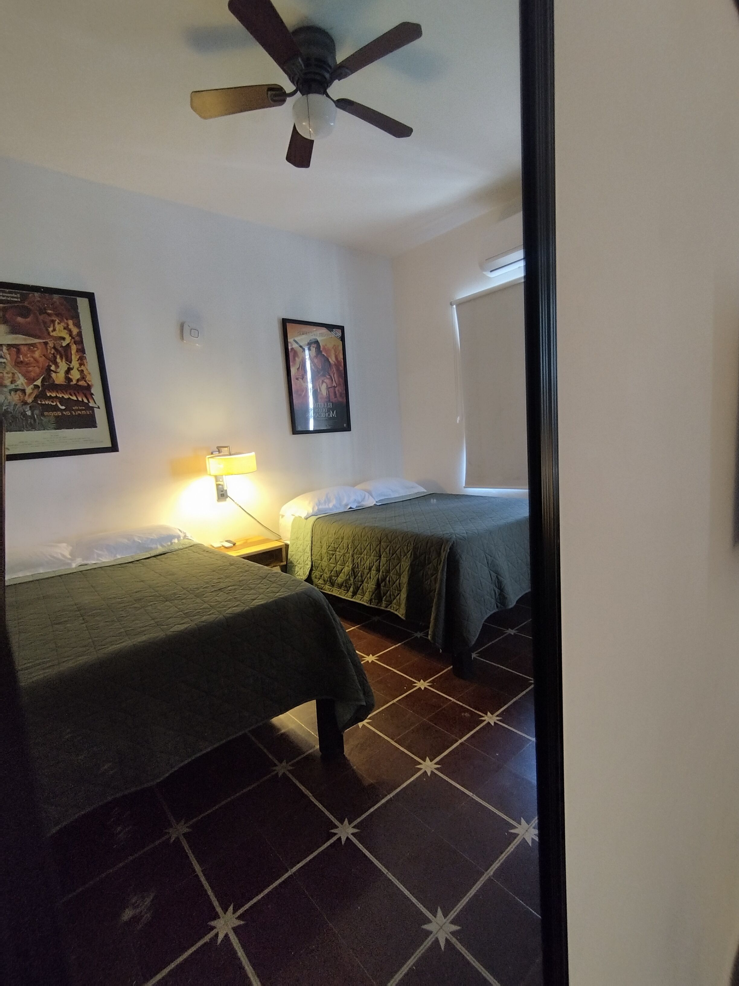 Ein Hotelzimmer mit zwei Betten, einem Deckenventilator, einer Nachttischlampe und einem gerahmten Bild an der Wand.