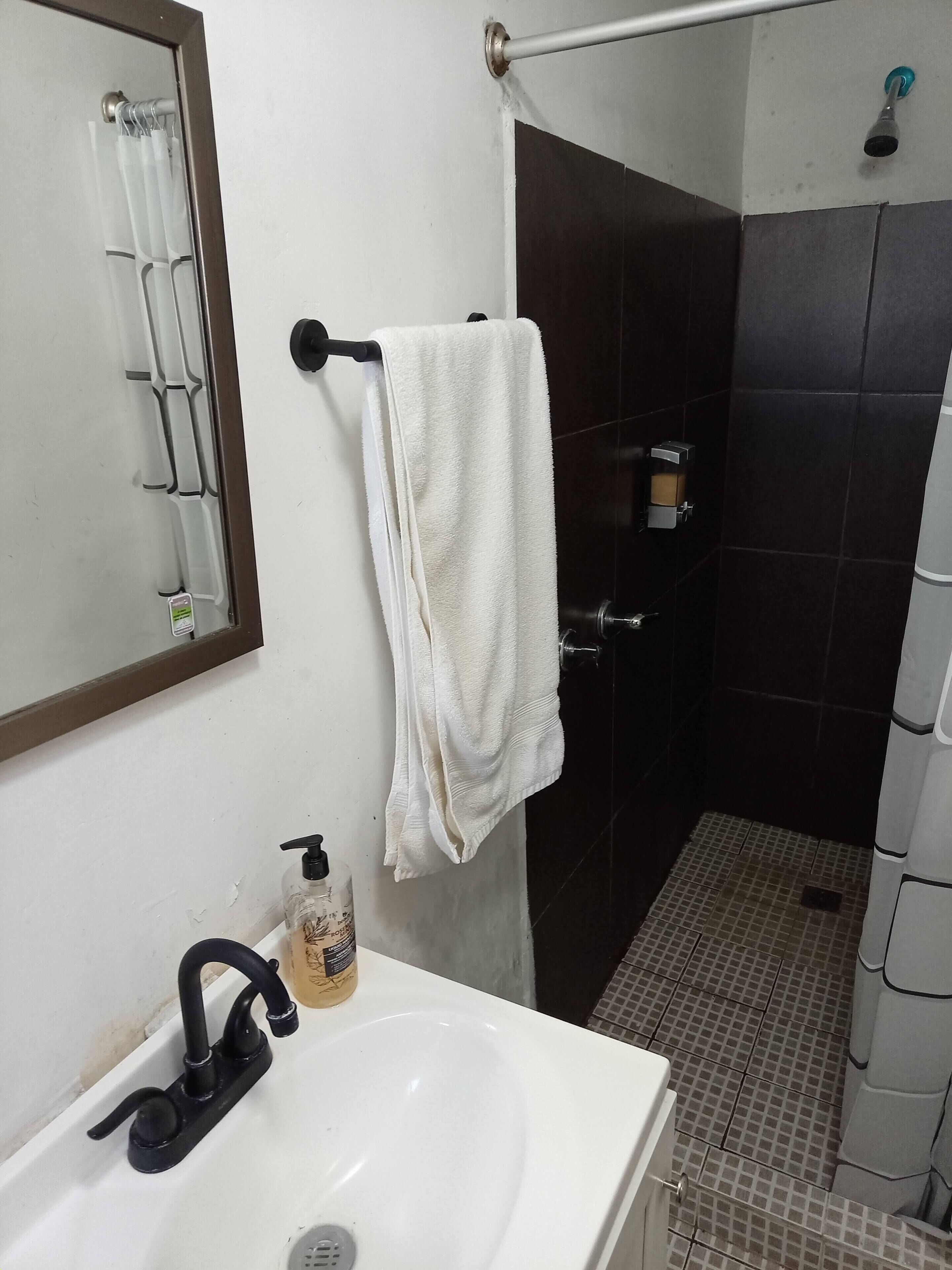 A bathroom with a white sink, a black faucet, a towel hanging on a rack, a soap dispenser, and a shower area with dark tiles.