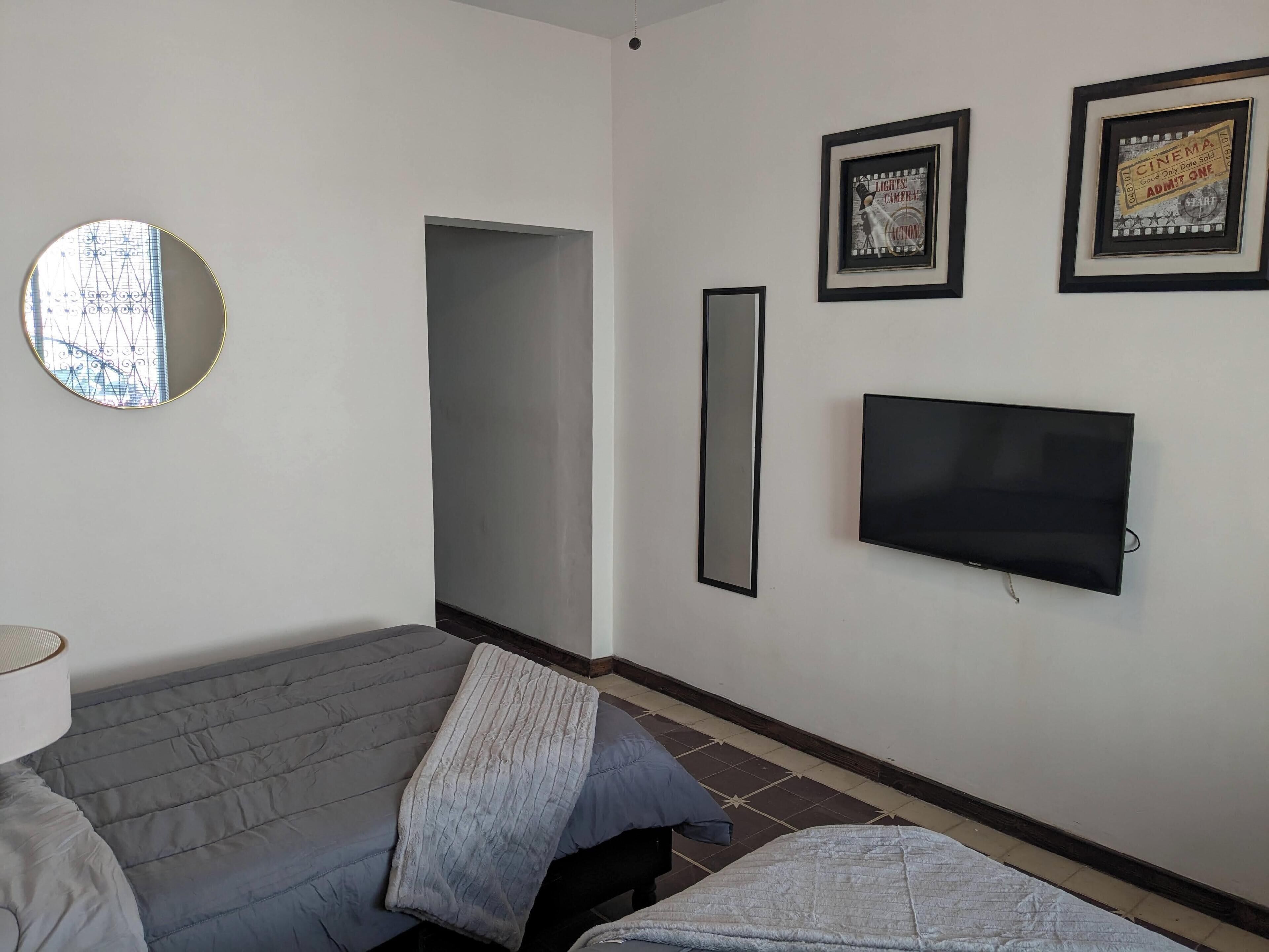 Ett rum med en grå soffa, en tv som är monterad på väggen och två inramade tavlor ovanför tv:n.