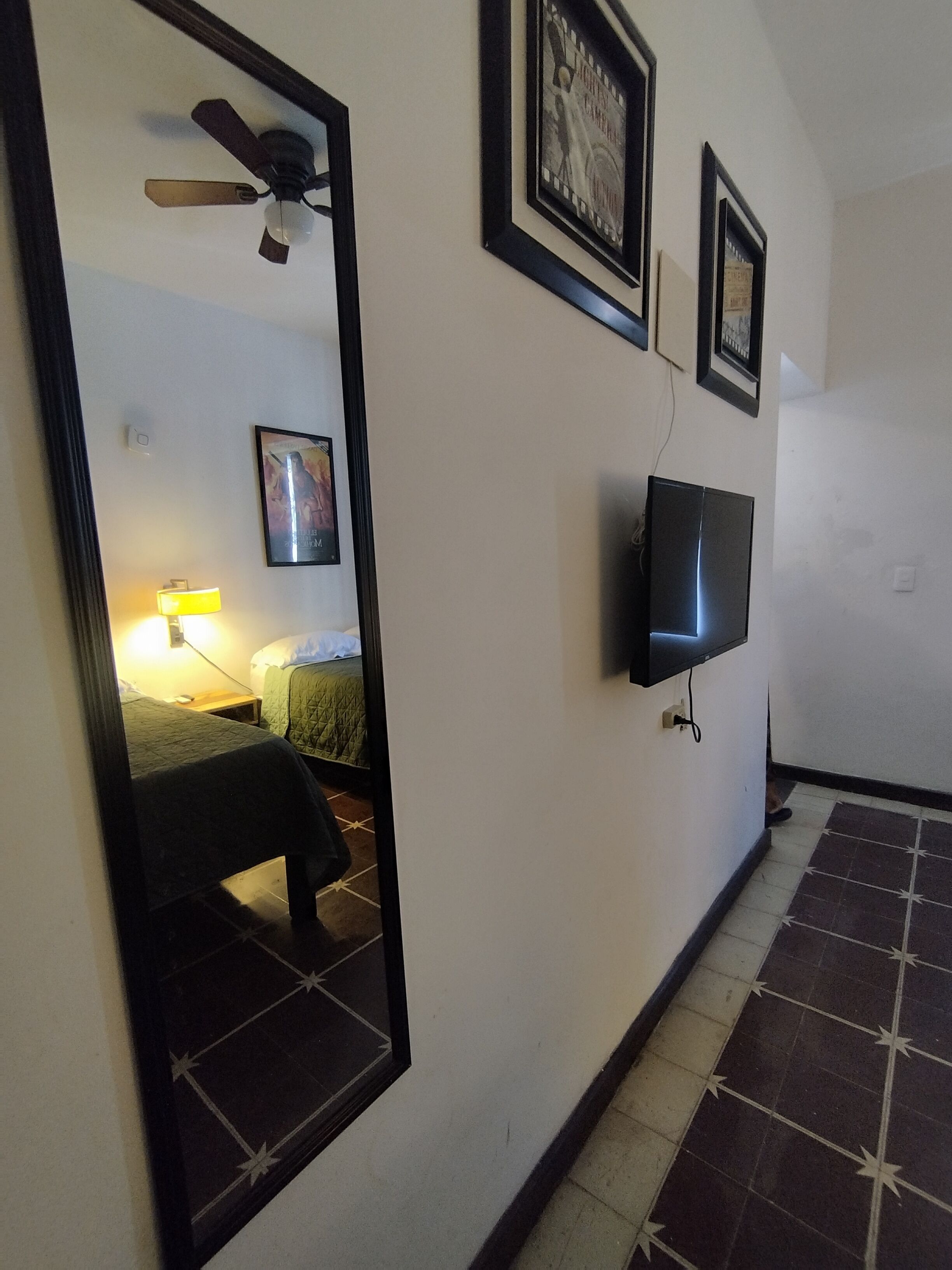 A hotel room with a bed, a TV mounted on the wall, a ceiling fan, and a mirror reflecting part of the room.