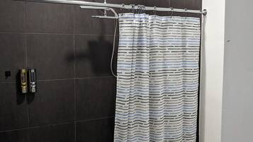 A bathroom with a shower, dark tiled walls, a striped shower curtain, a metal bucket, and a toilet.